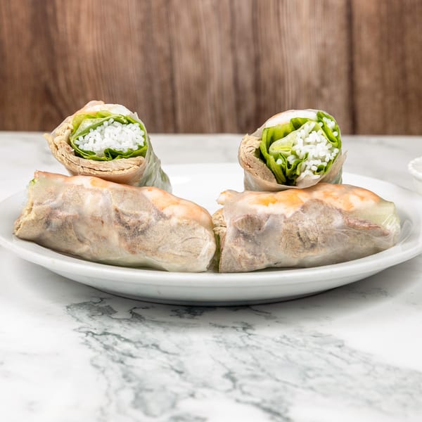 Four fresh Vietnamese spring rolls with shrimp, pork, rice, and lettuce on a white plate.
