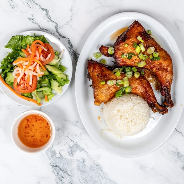 Vietnamese grilled chicken with rice, a side salad, and dipping sauce on a marble surface.