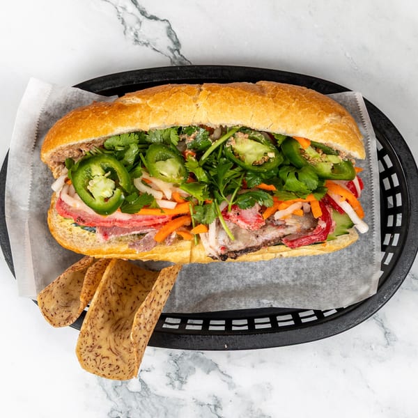 A vibrant Bánh Mì Hội An sandwich, overflowing with meats, pickled vegetables, cilantro, and jalapeños.