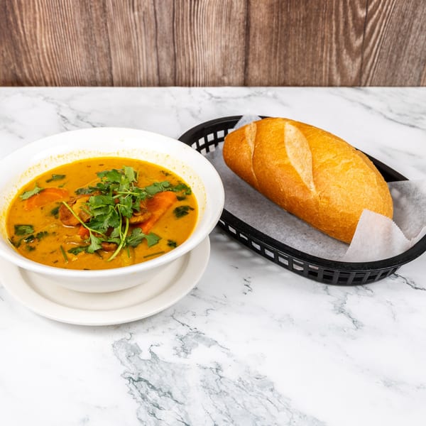 Vietnamese curry with chicken, carrots, and cilantro in a white bowl, served with a baguette.