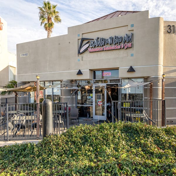 Exterior of Bánh Mì Hội An, a Vietnamese restaurant with outdoor seating and a palm tree.