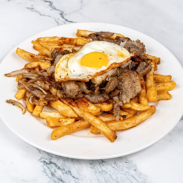 A plate of golden french fries topped with sliced beef, sautéed onions, and a fried egg.