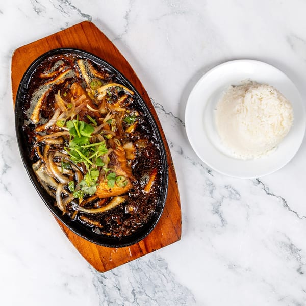 Sizzling Vietnamese fish in a dark sauce with onions and cilantro, served with white rice.